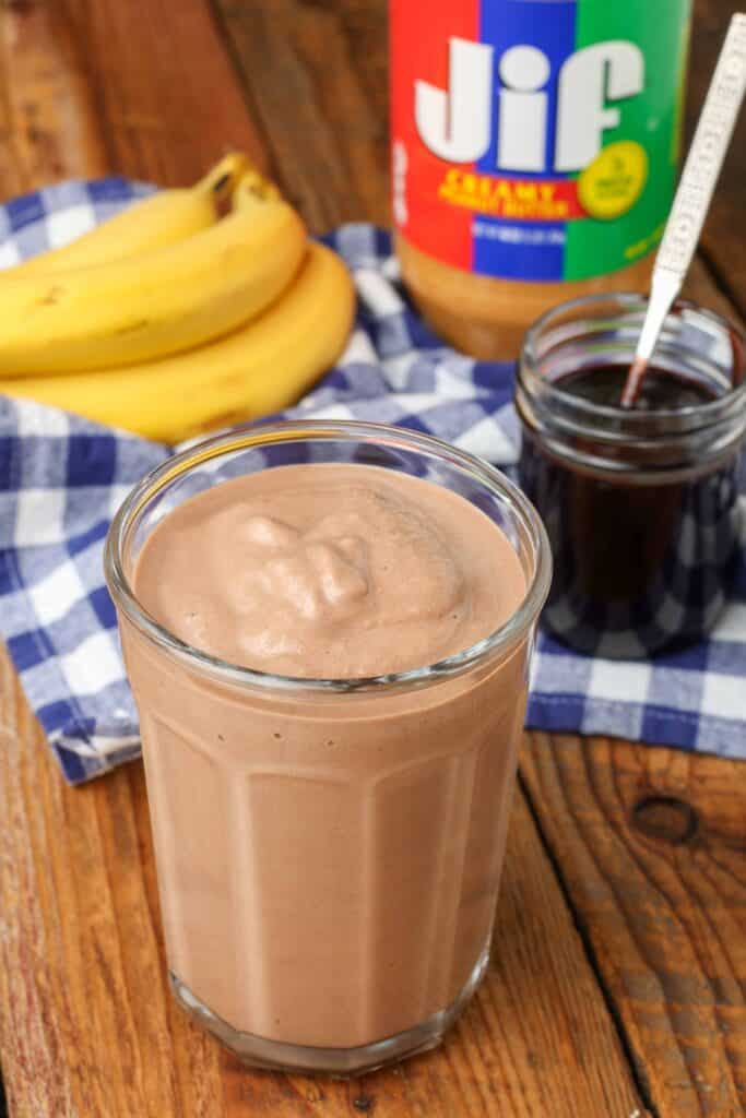 Chocoladesaus, een banaan en een pot pindakaas staan ​​op de achtergrond van deze foto van een smoothie